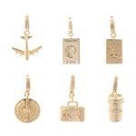 Gold-toned jewelry featuring six travel and leisure charms including an airplane, USA passport, Ace of Spades, compass with a clear gem, embossed suitcase, and coffee cup