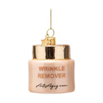 Glass ornament shaped like a light peachy-pink jar of "WRINKLE REMOVER Anti-Aging cream" with gold glitter accents, a shiny gold top, and a small gold star charm