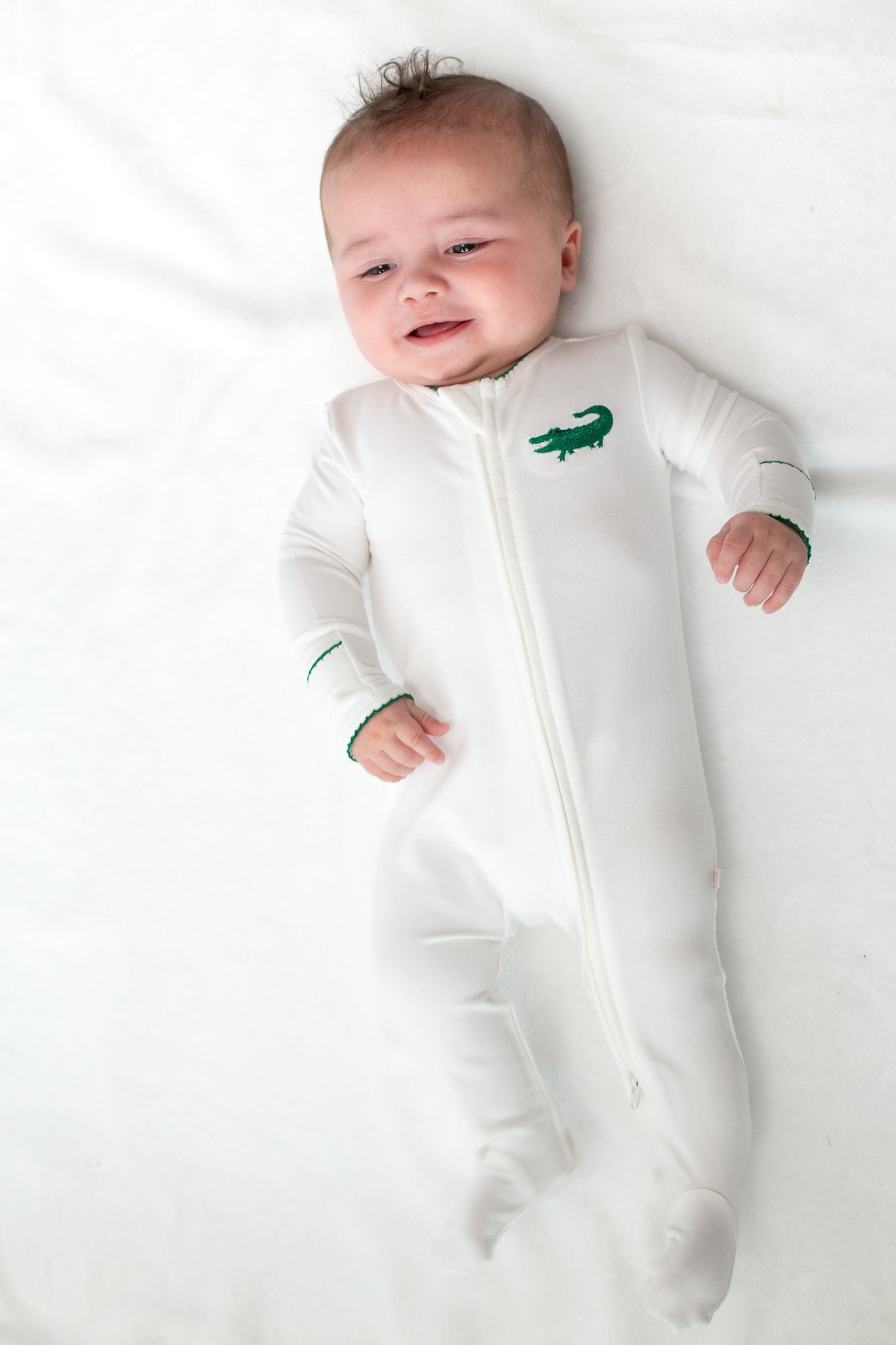 Baby wearing a white footed sleeper with a green alligator embroidery