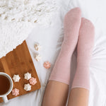 Person wearing pink fuzzy socks on a white bed with a wooden tray and small meringues