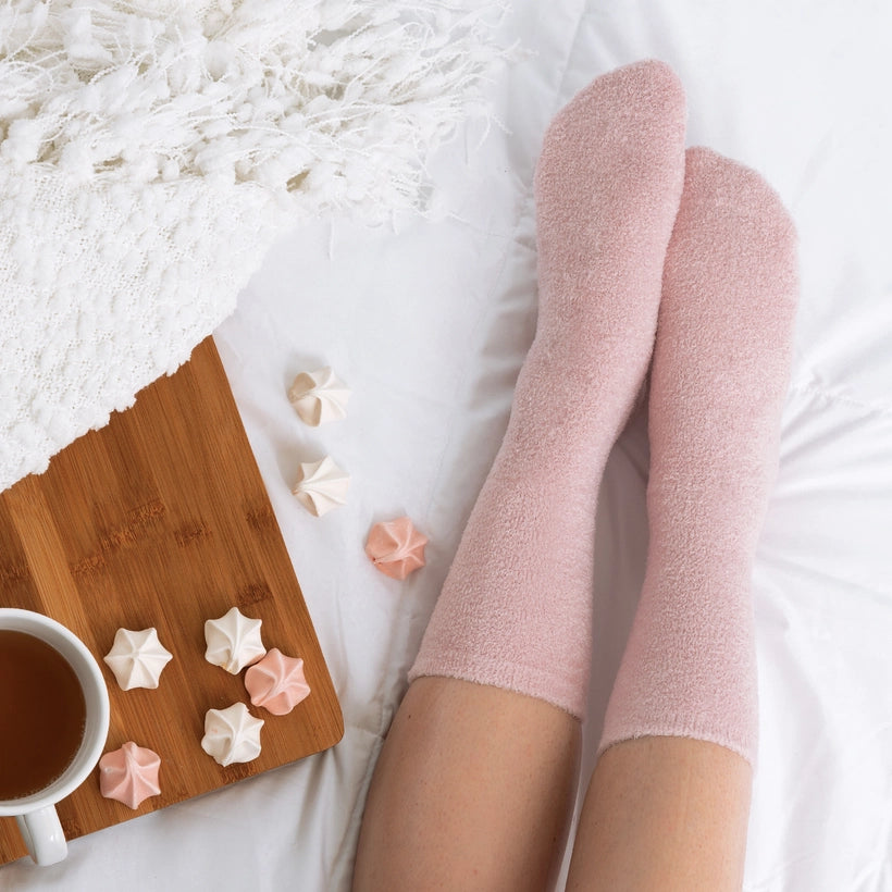 Person wearing pink fuzzy socks on a white bed with a wooden tray and small meringues