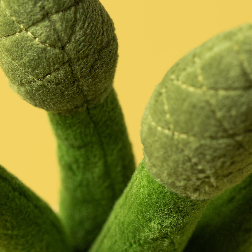 Close up of green felt asparagus stalks with stitched details against a yellow background