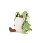 Plush toy of a cute potted plant character with a cream textured pot body, trailing green vine leaves, small brown corduroy feet, and tiny embroidered black eyes sitting on a white background