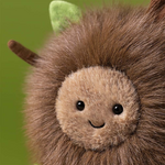 Close up of a round brown plush toy with a light brown face and small green leaf detail