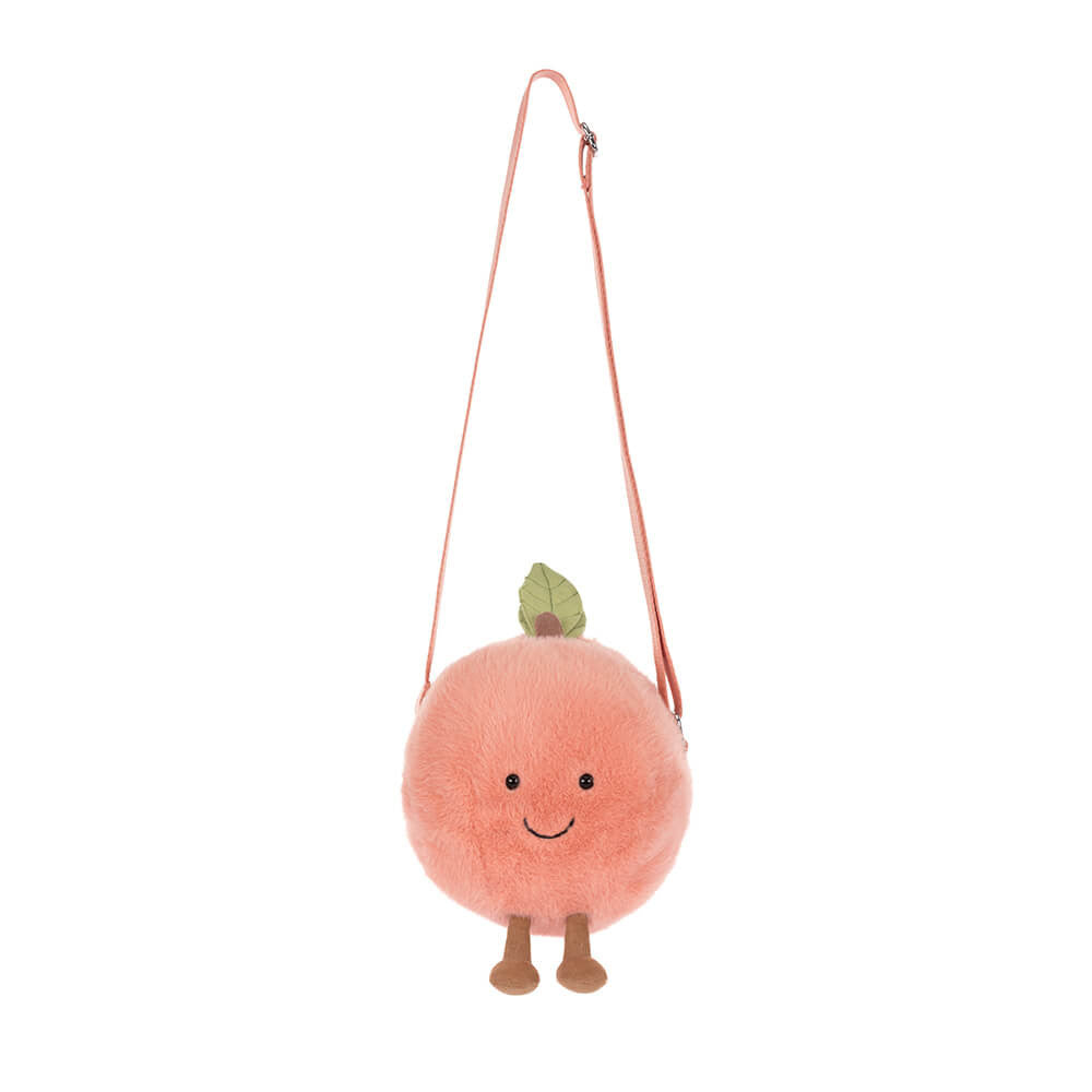 A fuzzy round peach-orange plush shoulder bag with a smiling embroidered face, a small green leaf, and tiny brown feet, suspended by a pink strap against a white background
