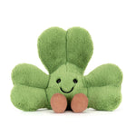 Plush toy of a fuzzy lime green shamrock with embroidered black eyes and a smiling mouth, featuring two ribbed brown corduroy feet, presented on a clean white background