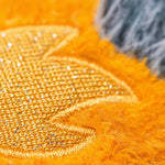 Macro photograph of a shimmering gold metallic embroidered motif on a vibrant orange fuzzy plush surface with soft grey faux fur accents
