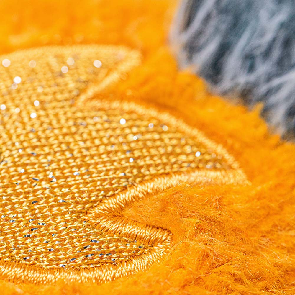 Macro photograph of a shimmering gold metallic embroidered motif on a vibrant orange fuzzy plush surface with soft grey faux fur accents