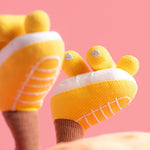 Yellow baby booties with white soles and embroidered toe details on a pink background