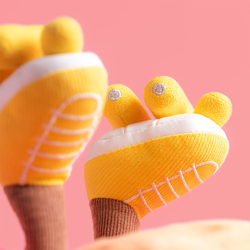 Yellow baby booties with white soles and embroidered toe details on a pink background