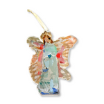 Mixed media collage ornament by L. Dyann depicting a stylized angel in a mint green and abstract blue patchwork dress, with textured gold and peach wings, a golden halo, and a cream hanging ribbon