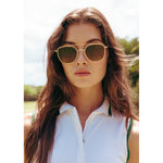 woman wearing gold aviator sunglasses with brown lenses standing in the outdoors