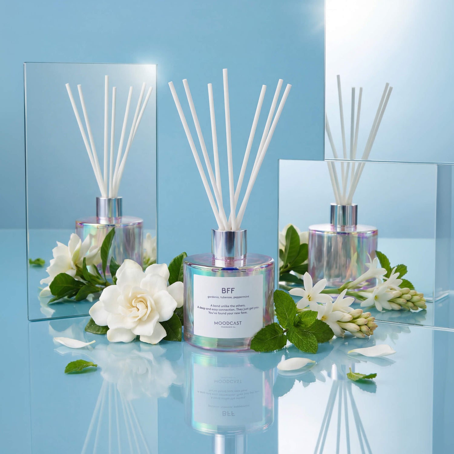 BFF reed diffuser with gardenia and tuberose flowers and mint leaves on a blue reflective surface
