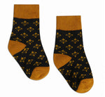 Textile pair of black socks featuring a repeating gold fleur-de-lis pattern with mustard yellow ribbed cuffs, heels, and toes