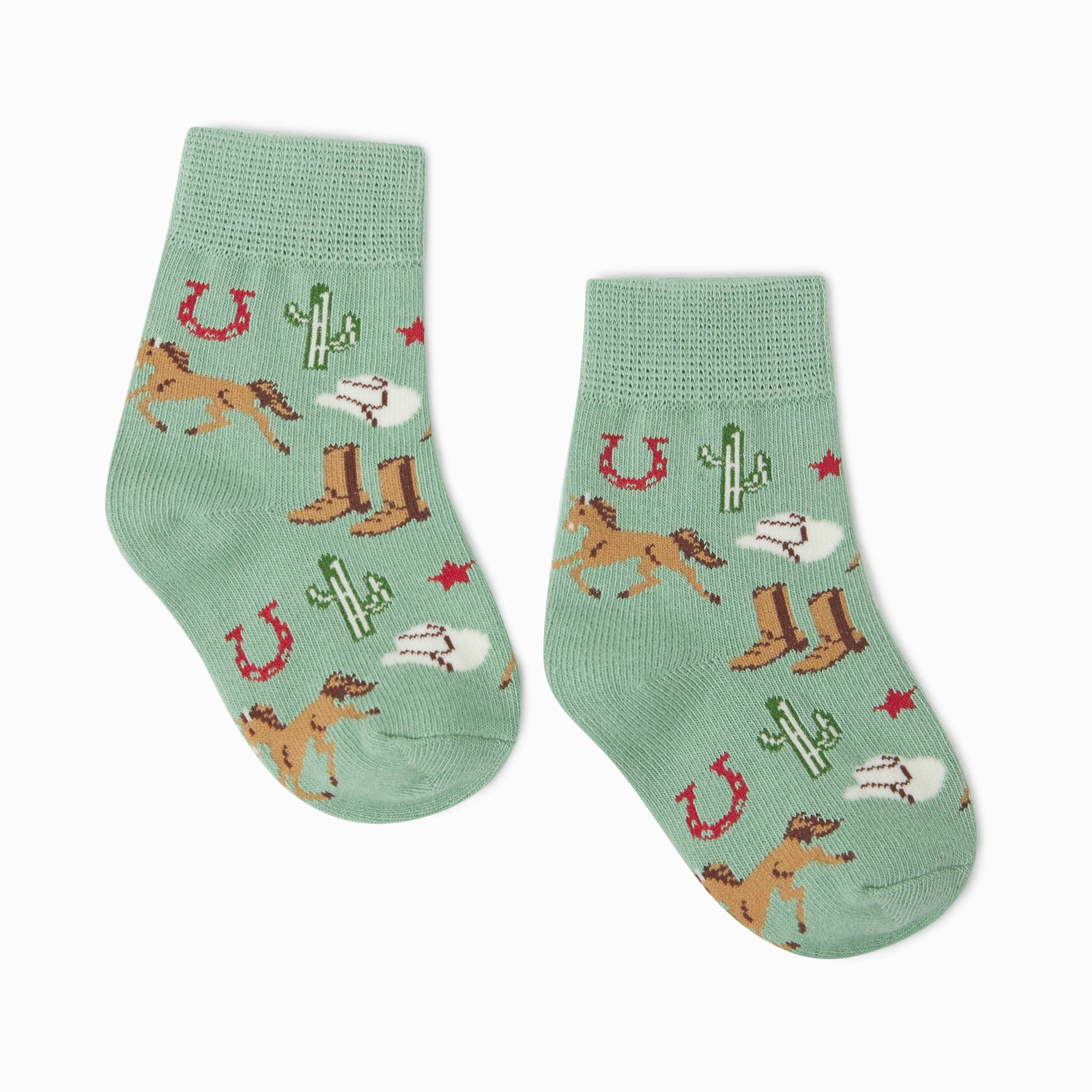 Knitted textile children's socks featuring a vibrant Western pattern of galloping brown horses, green saguaro cactuses, brown cowboy boots, red horseshoes, and red stars on a soft mint green background