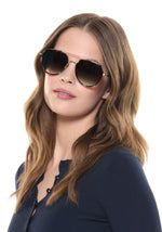 Photograph of a young woman with long wavy light brown hair wearing oversized tortoise-shell aviator sunglasses with gradient brown lenses and a navy blue ribbed cardigan with white buttons against a white studio background