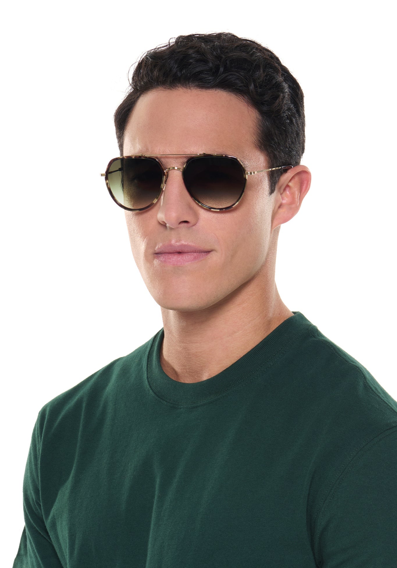 A man with dark hair wearing tortoiseshell aviator sunglasses with gradient lenses and a dark green crew neck t-shirt in a studio setting