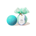 Musee two bath bombs one unwrapped vibrant turquoise and one wrapped in crinkled mint green tissue paper featuring a 'Sweet Dreams Surprise Bath Balm' tag secured with gold string