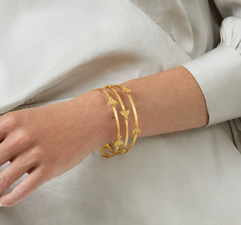 Three gold bangles with bee motifs worn on a wrist