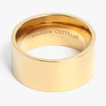Gold ring by Marrin Costello a wide polished flat band featuring the brand name engraved on the interior surface