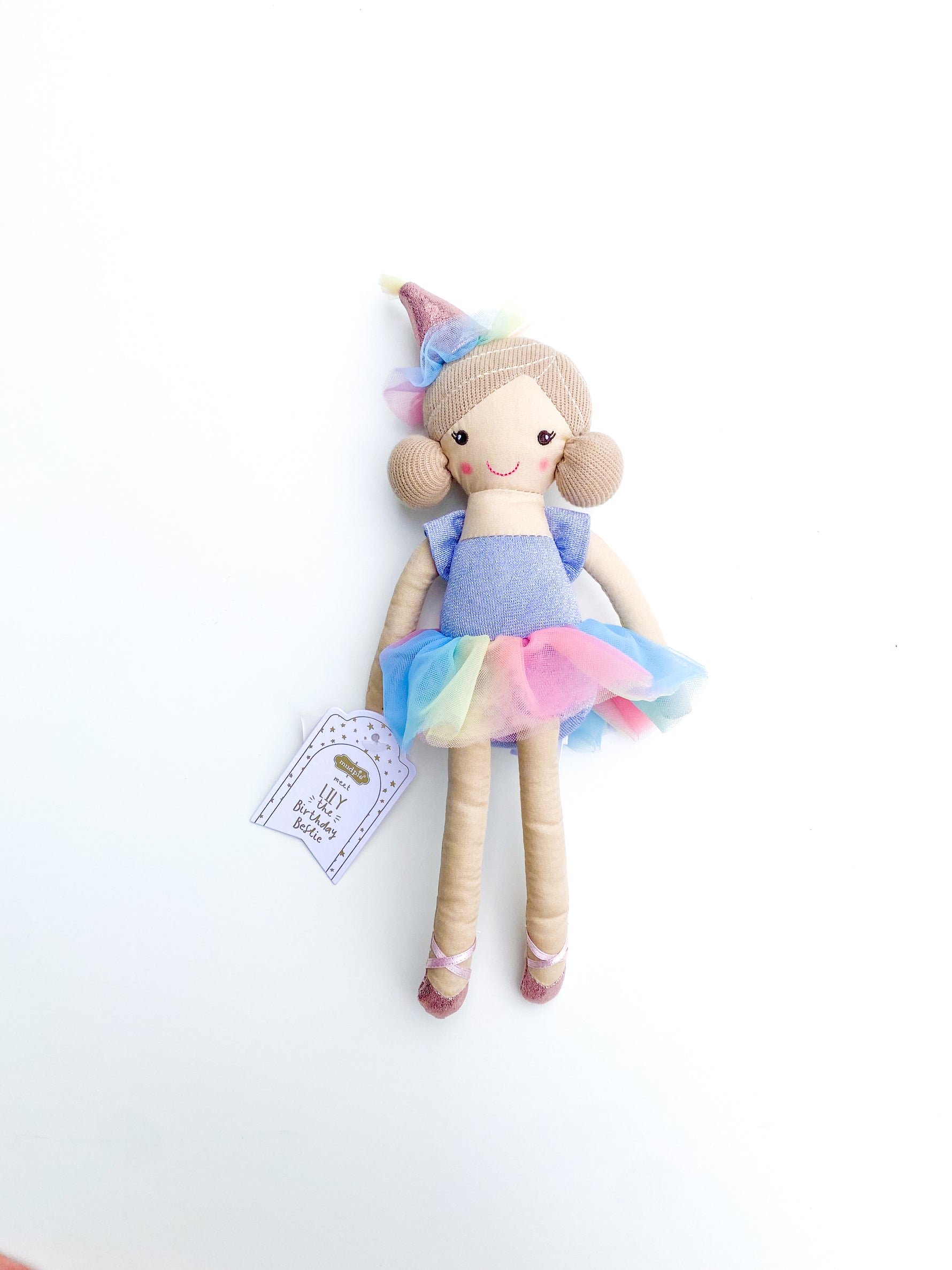 Mudpie plush doll Lily the Birthday Bestie on a white background wearing a colorful rainbow tutu, a shimmering pink birthday hat, and sparkly pink ballet slippers