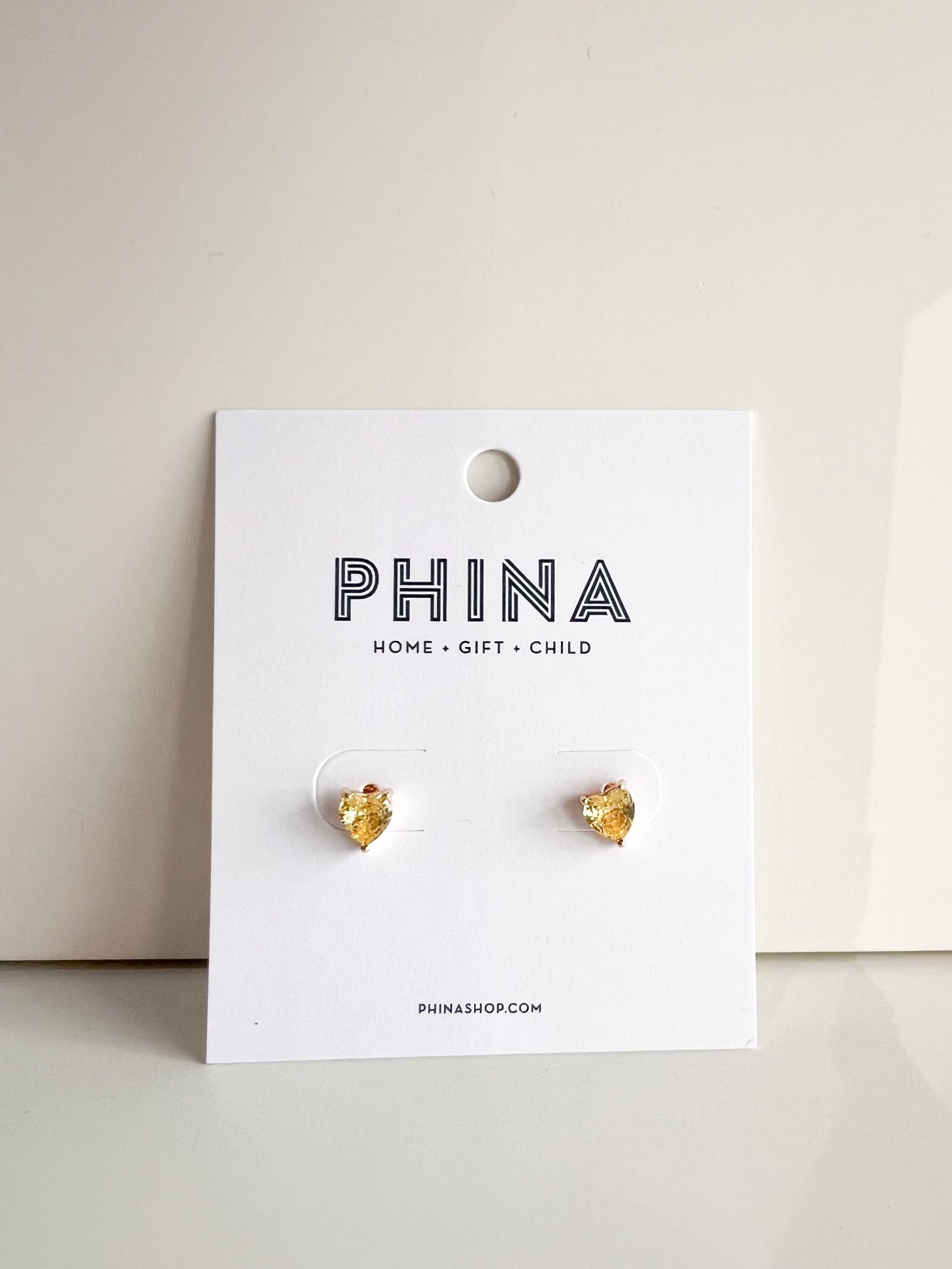 Yellow heart shaped stud earrings on a Phina branded display card