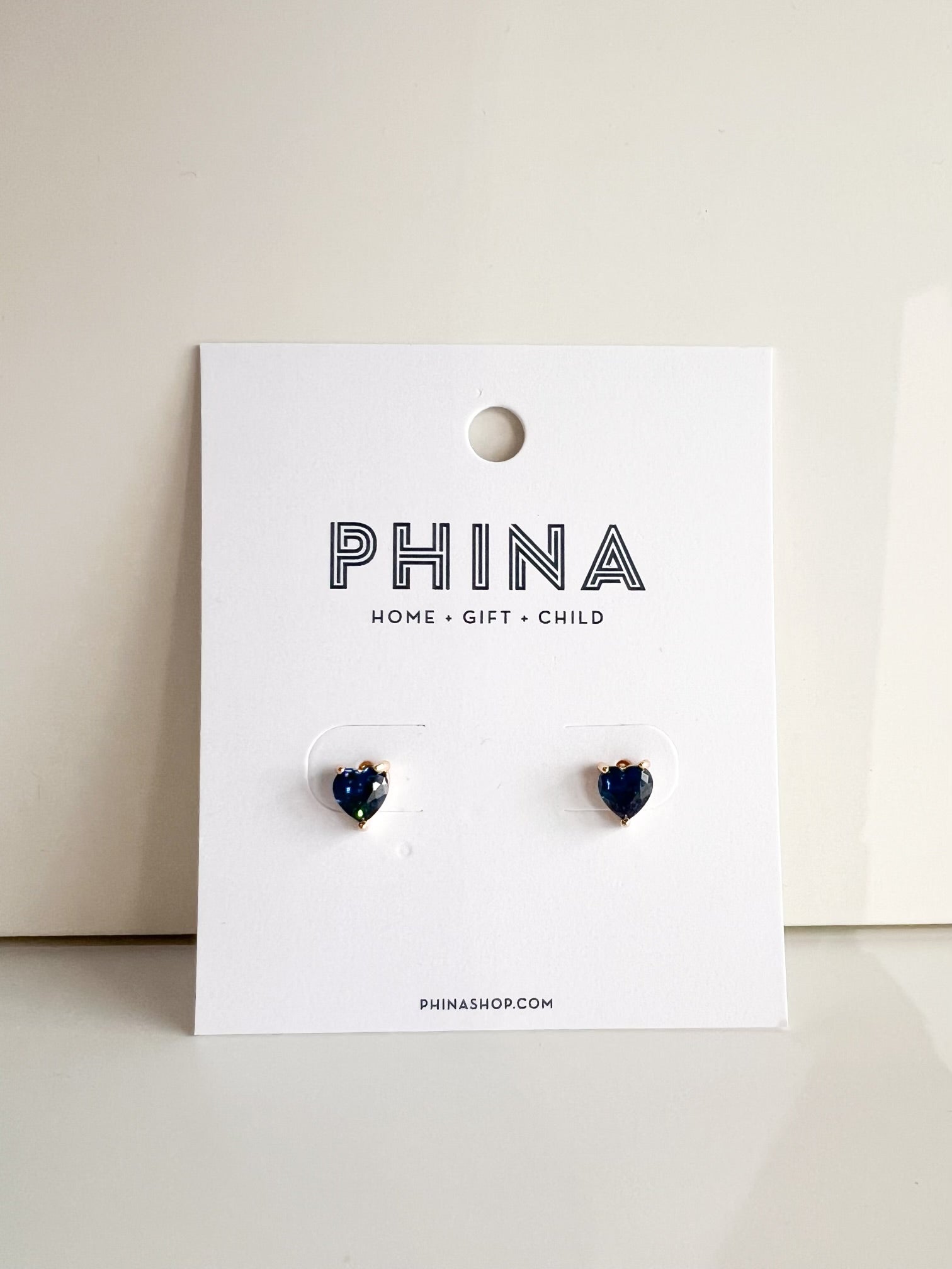 Pair of dark blue heart shaped stud earrings on a Phina branded display card