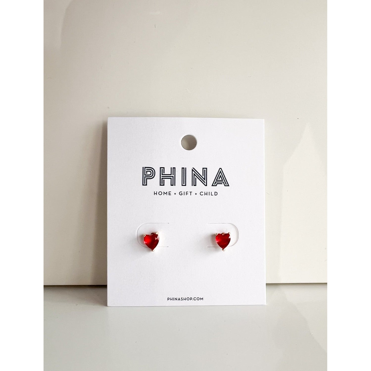 Red heart shaped stud earrings on a Phina branded display card