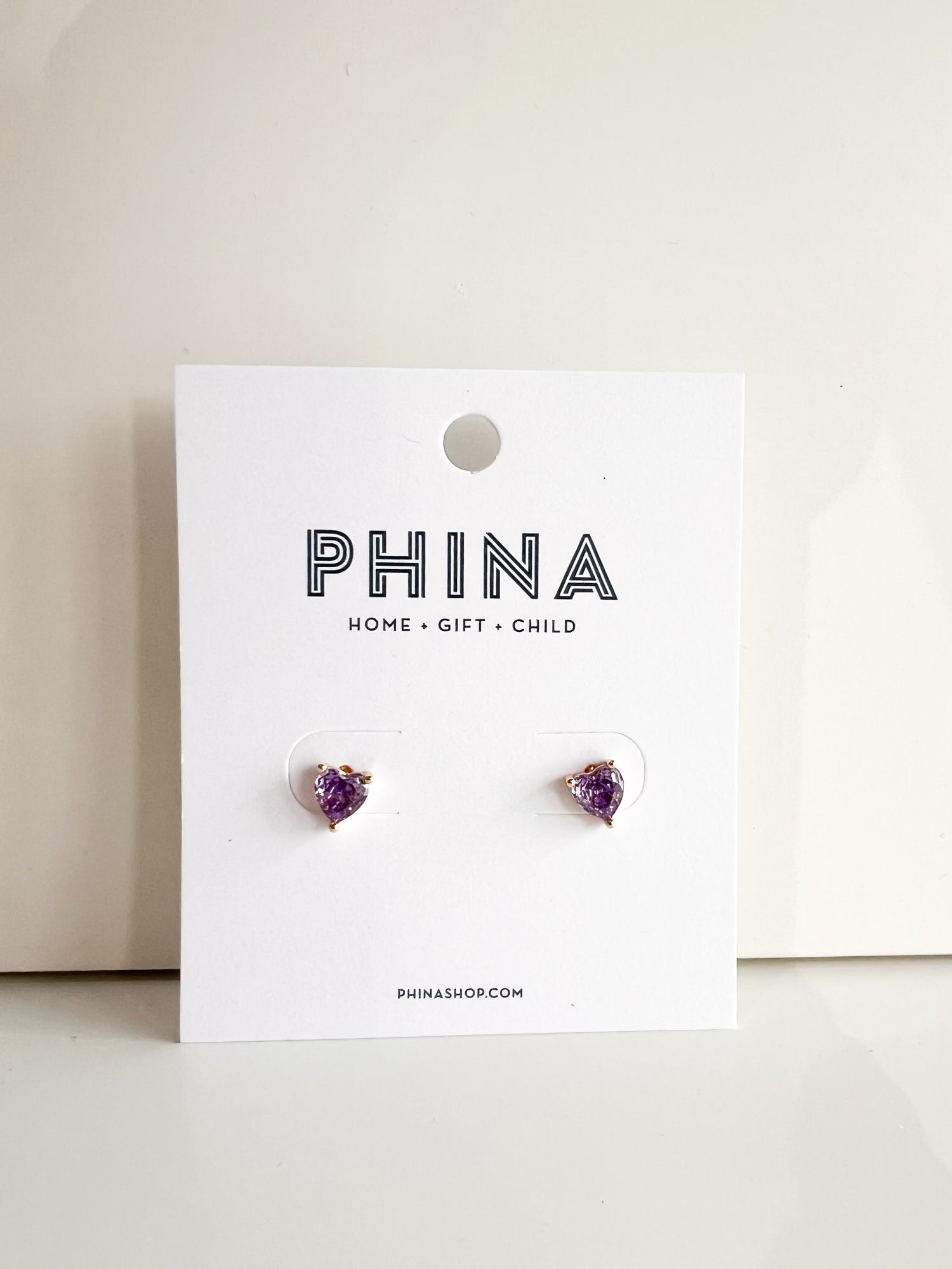 Pair of purple heart shaped stud earrings on a Phina branded display card
