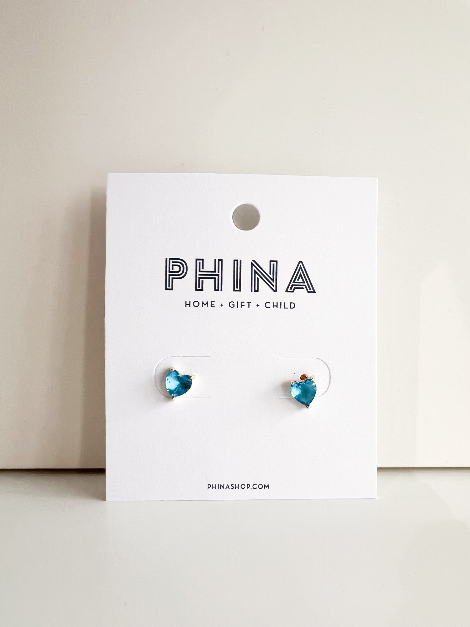 Blue heart shaped stud earrings on a Phina branded display card