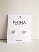 Gold heart shaped stud earrings with clear stones on a Phina branded display card