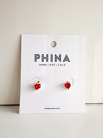 Gold stud earrings with red heart shaped crystals on a white display card