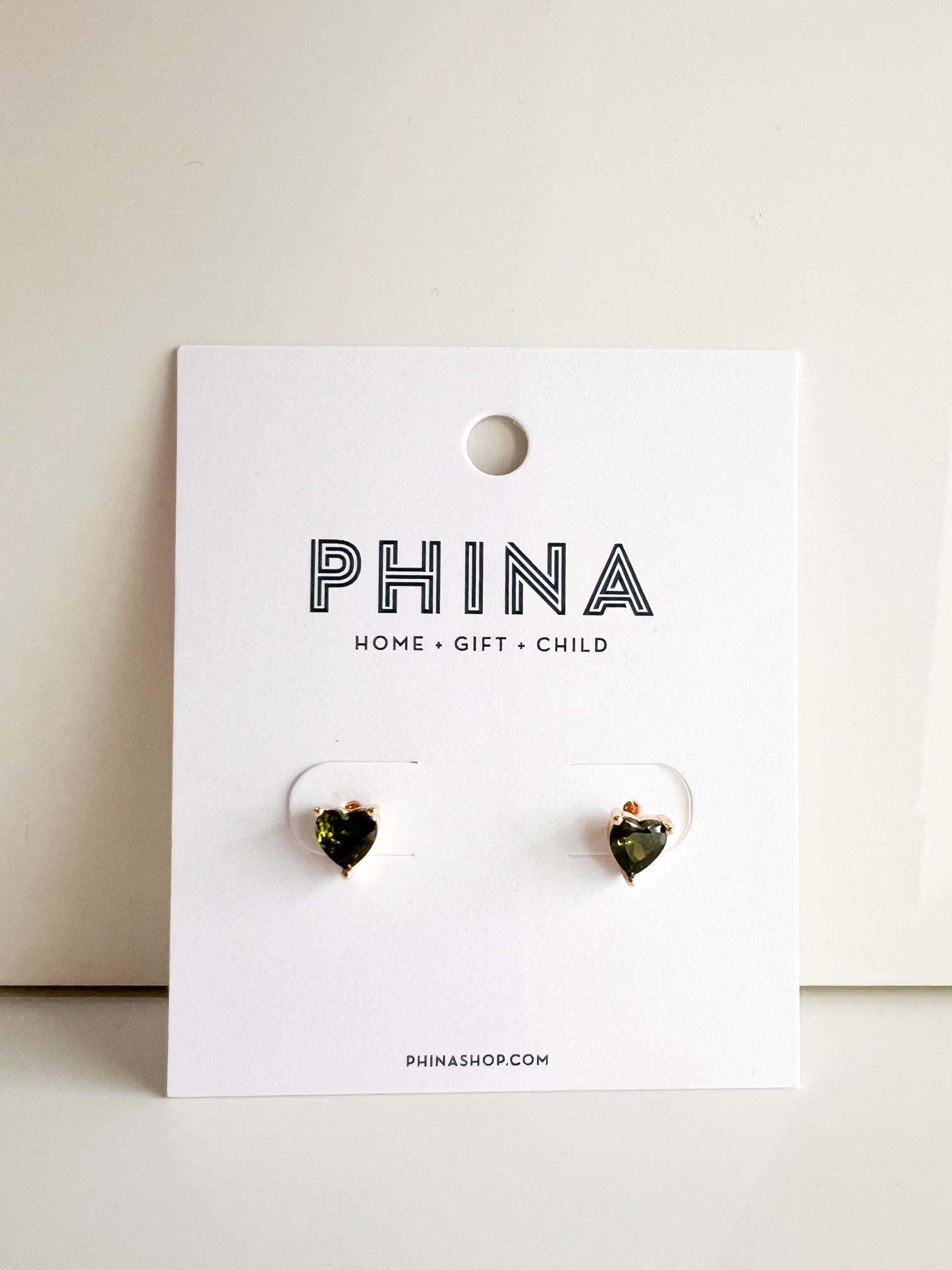 Pair of heart shaped green stone stud earrings on a white display card