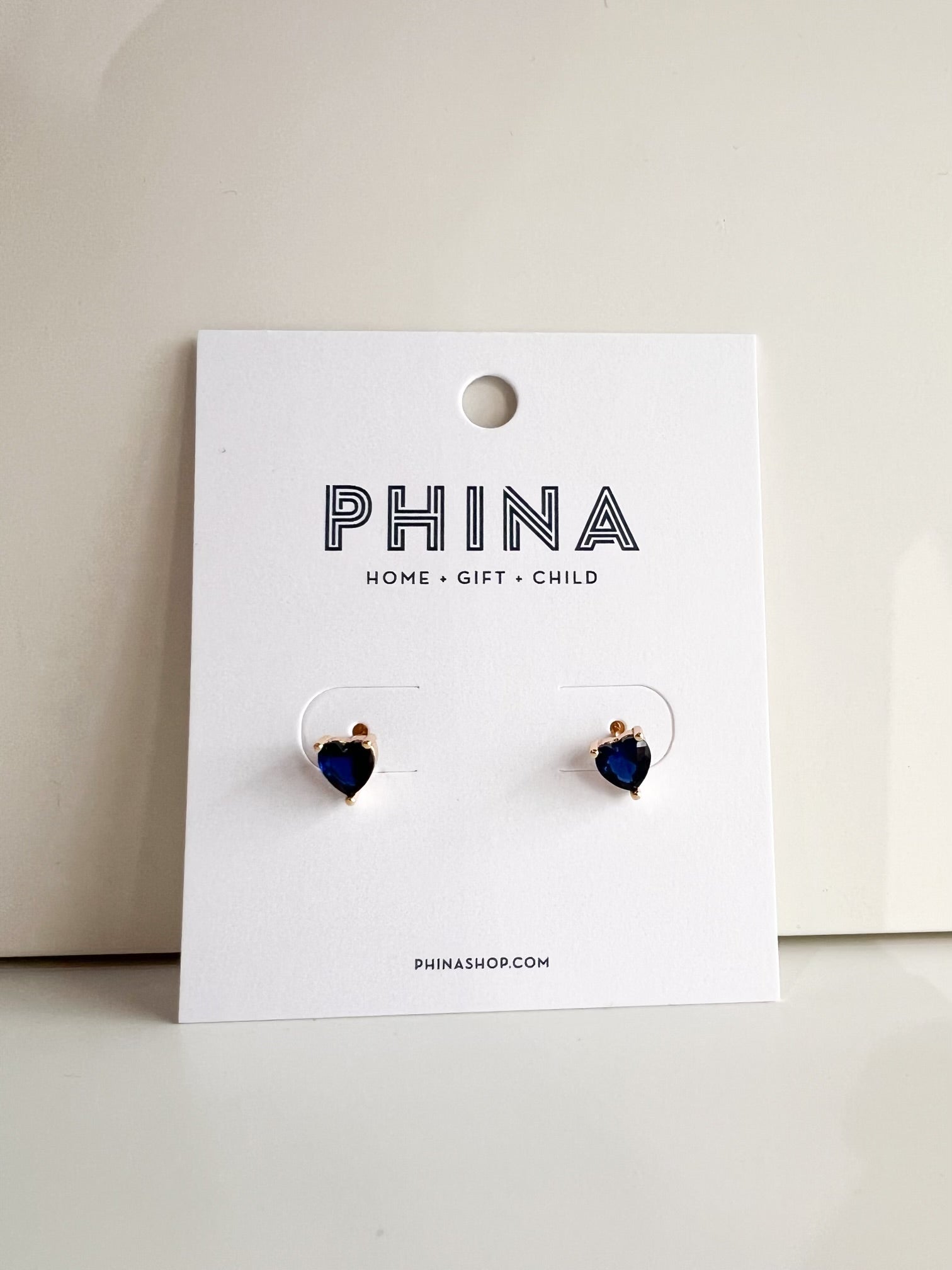 Pair of gold heart shaped blue stud earrings on a Phina branded display card