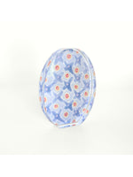 Clear glass dome paperweight featuring an internal pattern of light blue X-shapes interspersed with vibrant coral and yellow dots against a pale background