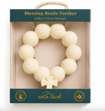 Cream colored circular rubber baby teether with cross charm in retail packaging