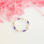 Bracelet with blue and gold beads on a white surface with pink decorative elements