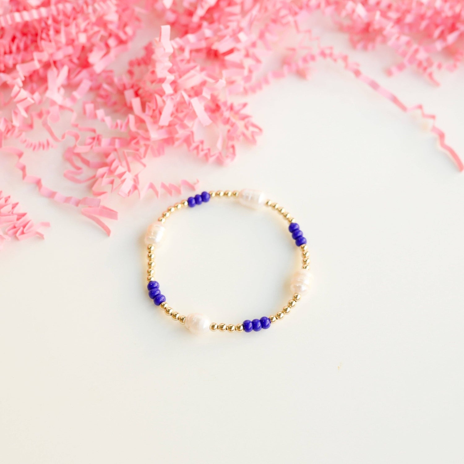 Bracelet with blue and gold beads on a white surface with pink decorative elements