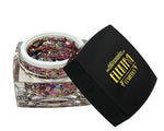 Digital photography by Elektracosmetics of an open clear jar filled with chunky iridescent cosmetic glitter shimmering in purple pink gold and blue-green hues, its black lid featuring the golden Elektracosmetics logo and lightning bolt symbol resting beside it on a white background