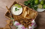 Bowl of creamy dip with lime and cilantro in a basket with tortilla chips
