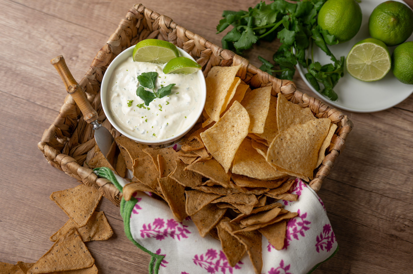 Bowl of creamy dip with lime and cilantro in a basket with tortilla chips