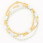Three delicate beaded bracelets featuring shiny gold spheres, translucent light blue faceted rectangle beads, and smaller opaque light blue round beads, with one bracelet adorned by a small square gold charm