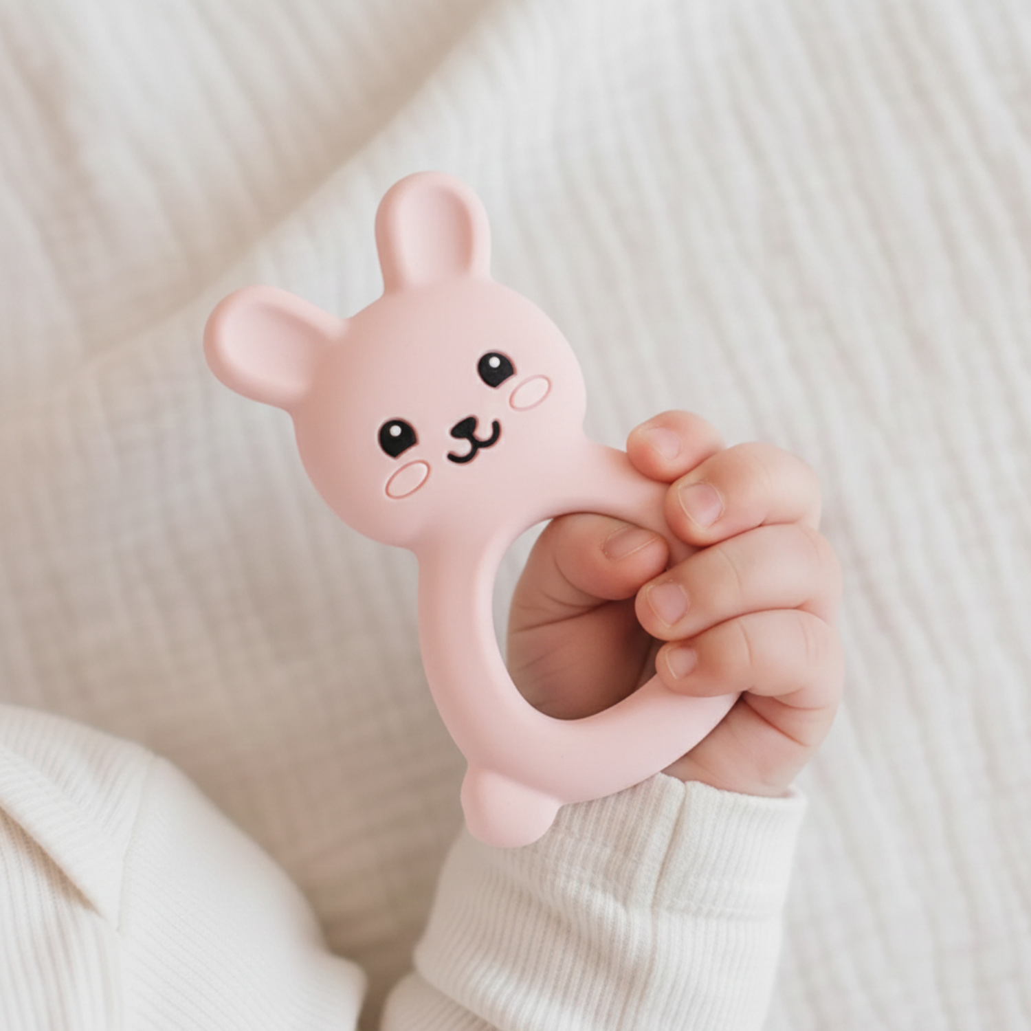 Baby hand holding a pink silicone rabbit shaped teether