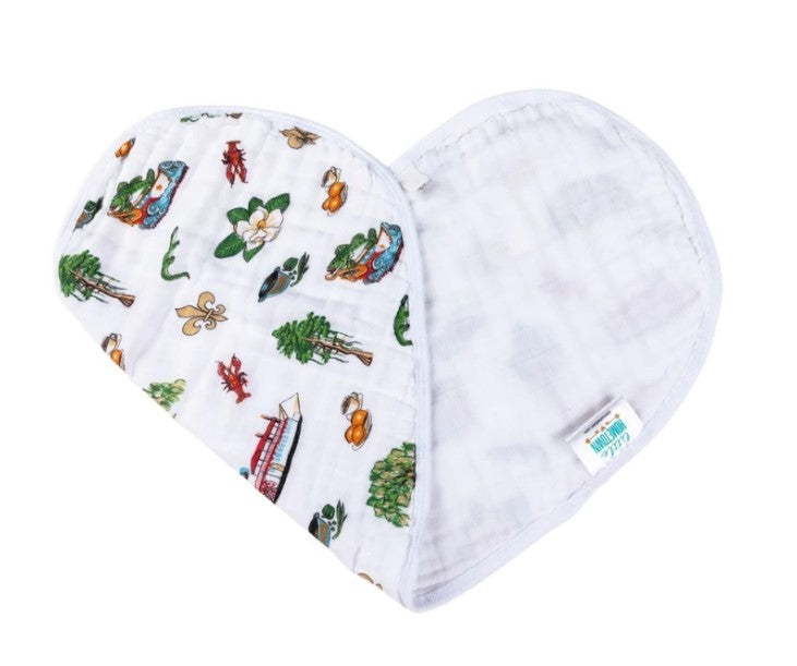 White cotton baby bib folded heart-shaped, patterned with colorful New Orleans and Louisiana icons like a gold fleur-de-lis, red crawfish, white magnolia, green alligators, and a red streetcar