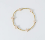 Gold beaded bracelet featuring evenly spaced light pink cross-shaped beads on a clean white background