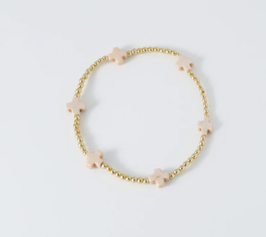 Gold beaded bracelet featuring evenly spaced light pink cross-shaped beads on a clean white background