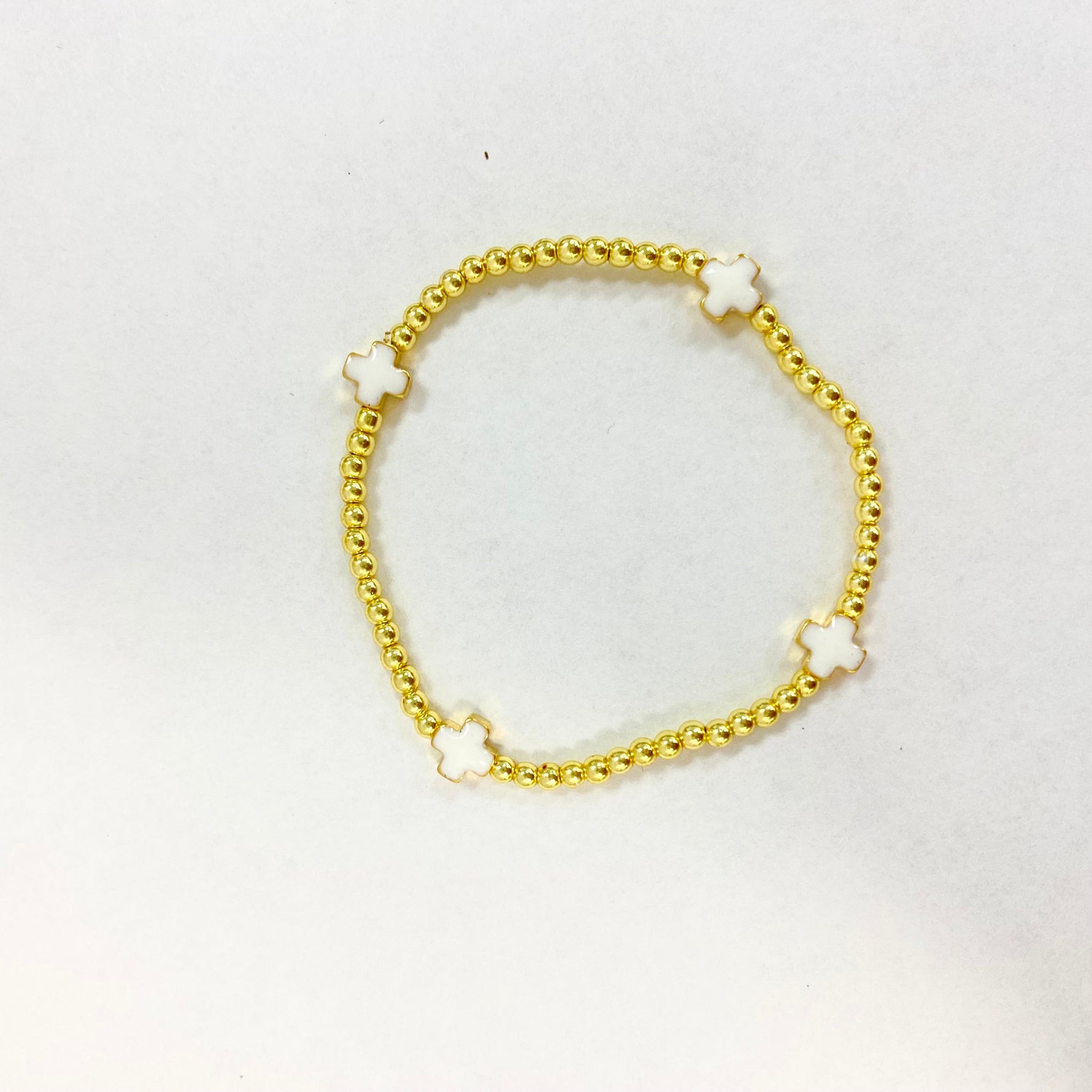 Photograph of a gold beaded bracelet featuring four small white enamel cross charms forming a circle on a bright white background