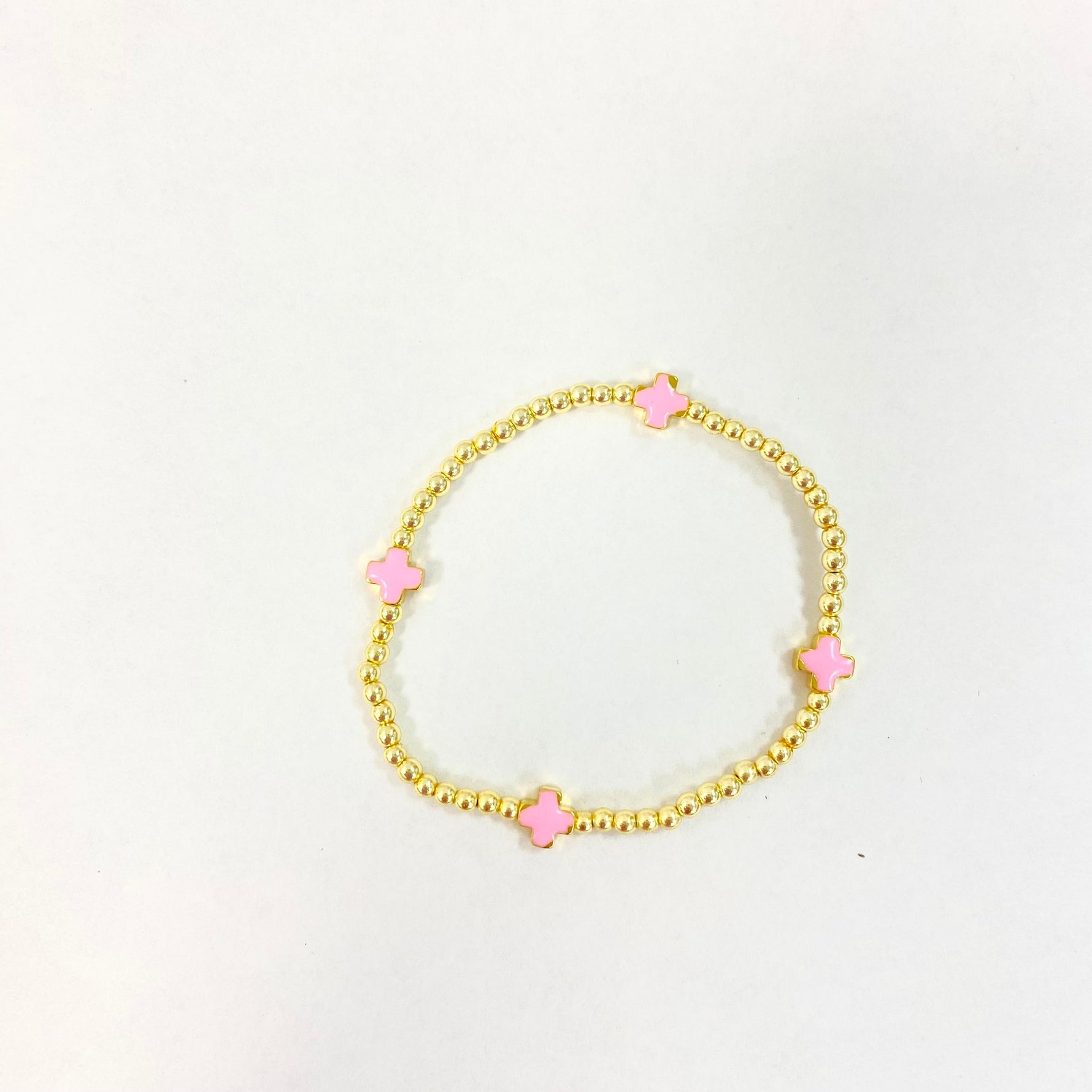Gold beaded stretch bracelet featuring four spaced pink enamel clover charms on a white background