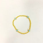 A gold beaded bracelet featuring four light blue cross charms on a plain white background