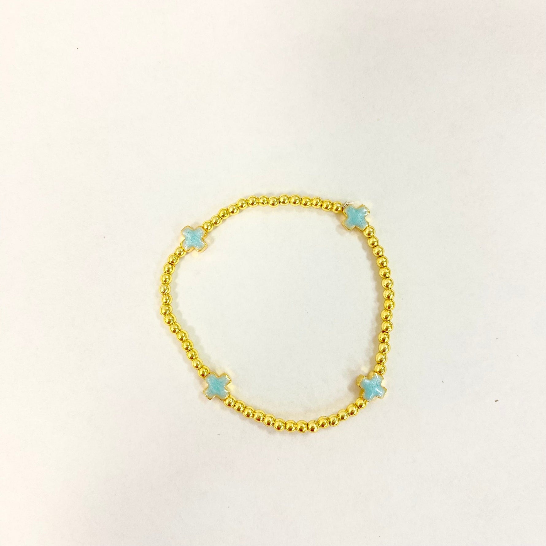 A gold beaded bracelet featuring four light blue cross charms on a plain white background